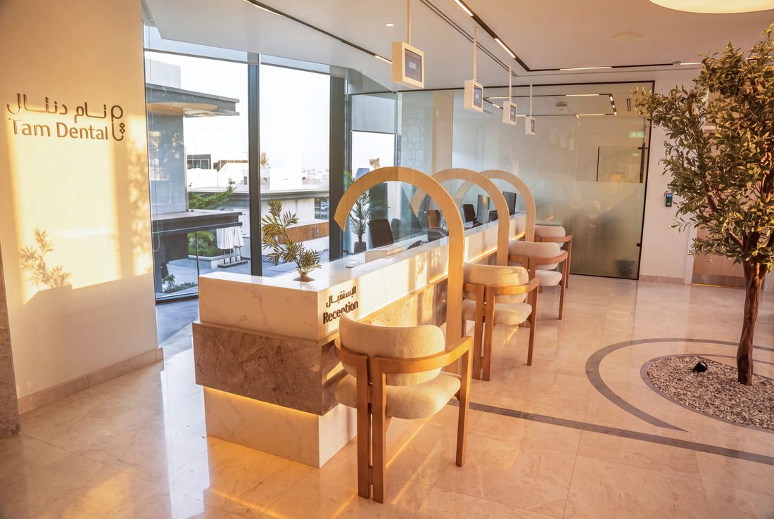 The Tam Dental front desk in Jeddah beneath the clinic sign, lit by a window wall.